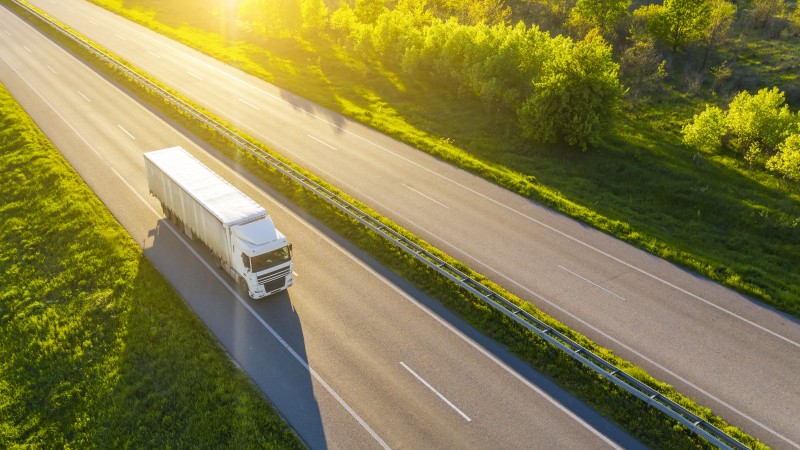 A white truck on a highway surrounded by a lush forest, bathed in the warm, soft light of the golden hour.